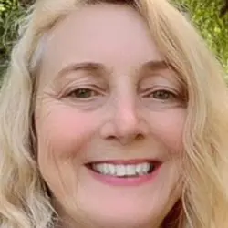 A headshot of Psychic Reader Grace, a woman with long blonde hair, smiling in front of trees.