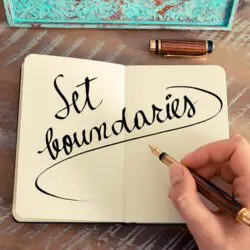 the words "set boundaries" in calligraphy written on a notebook